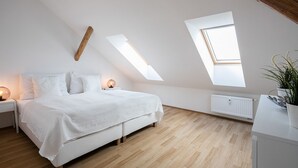 Une chambre avec un plafond en pente, des fenêtres de toit, un lit, des tables de chevet et un radiateur.