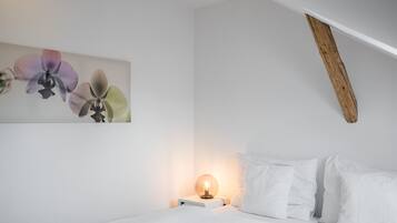 A bedroom with a bed, white pillows, a bedside table with a lamp, and a wall-mounted artwork of flowers.
