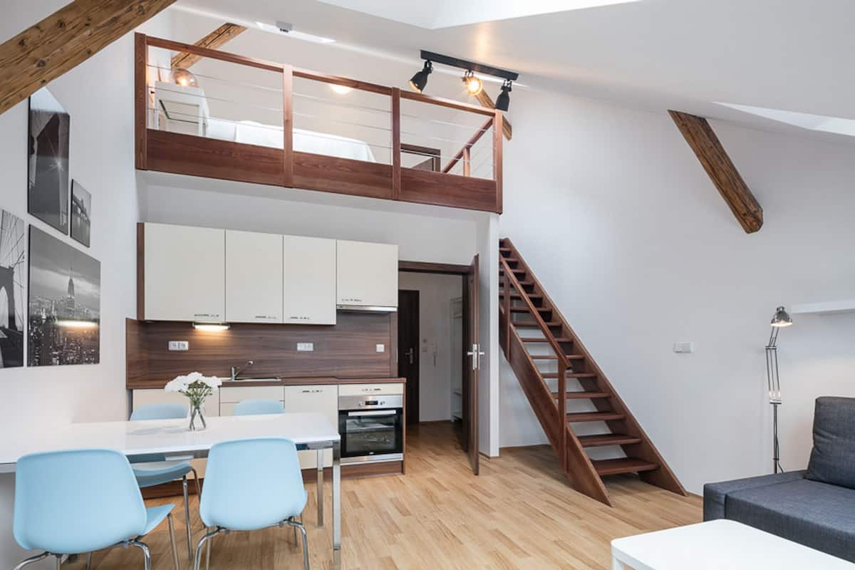 A modern loft apartment with a dining area, kitchen, and a wooden staircase.