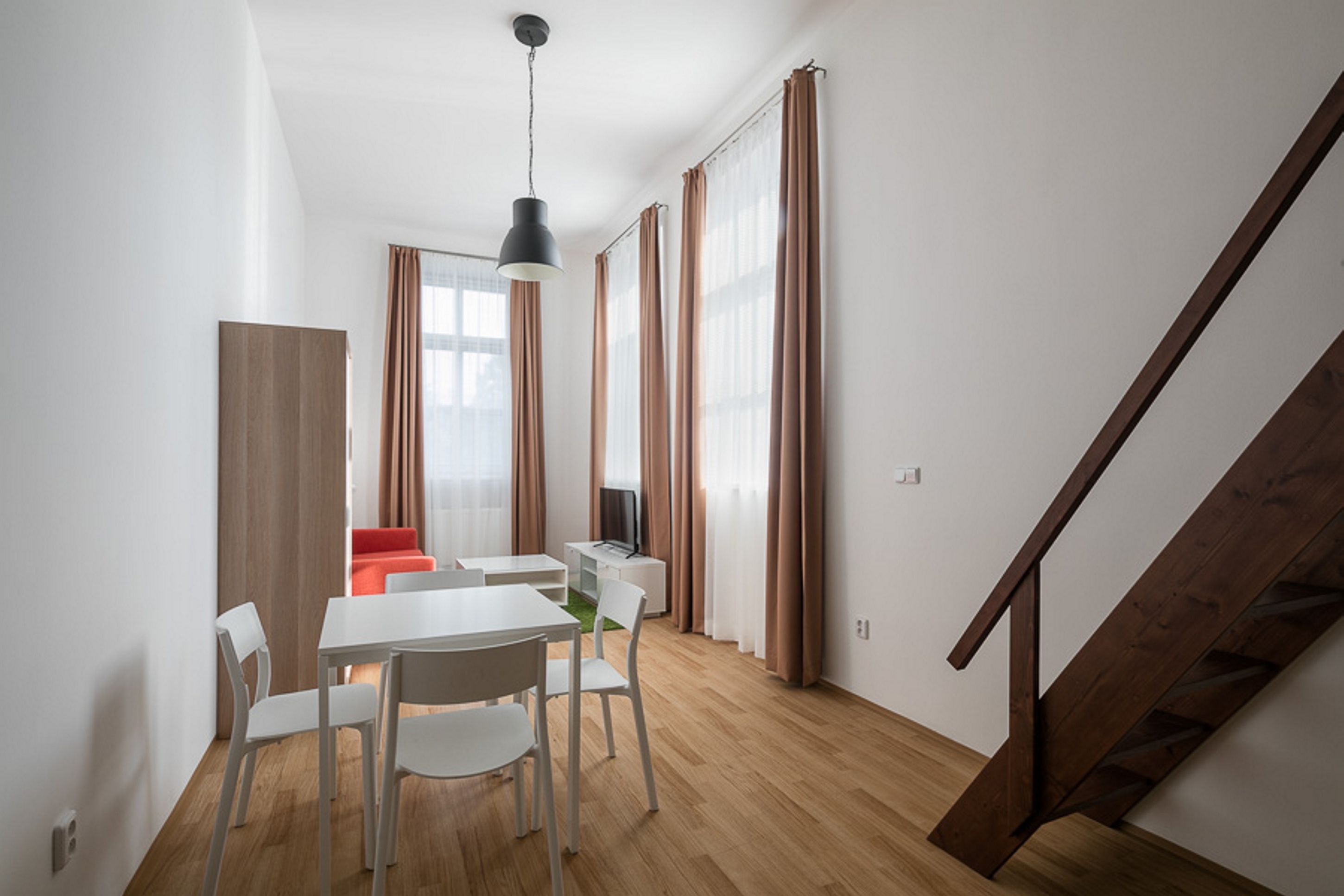 A modern living room with a dining area, wooden flooring, and a staircase.