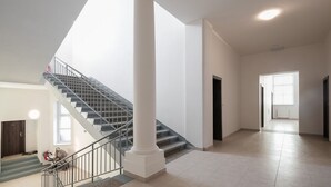 Un intérieur spacieux avec un escalier, de grandes colonnes et une vue sur une autre pièce.