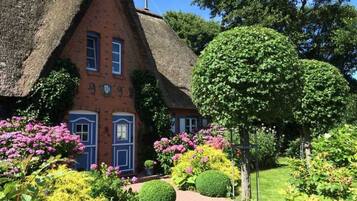 Ein traditionelles Haus mit Strohdach und Ziegelaußenwand, umgeben von gepflegten Gärten und einer Vielzahl blühender Pflanzen.