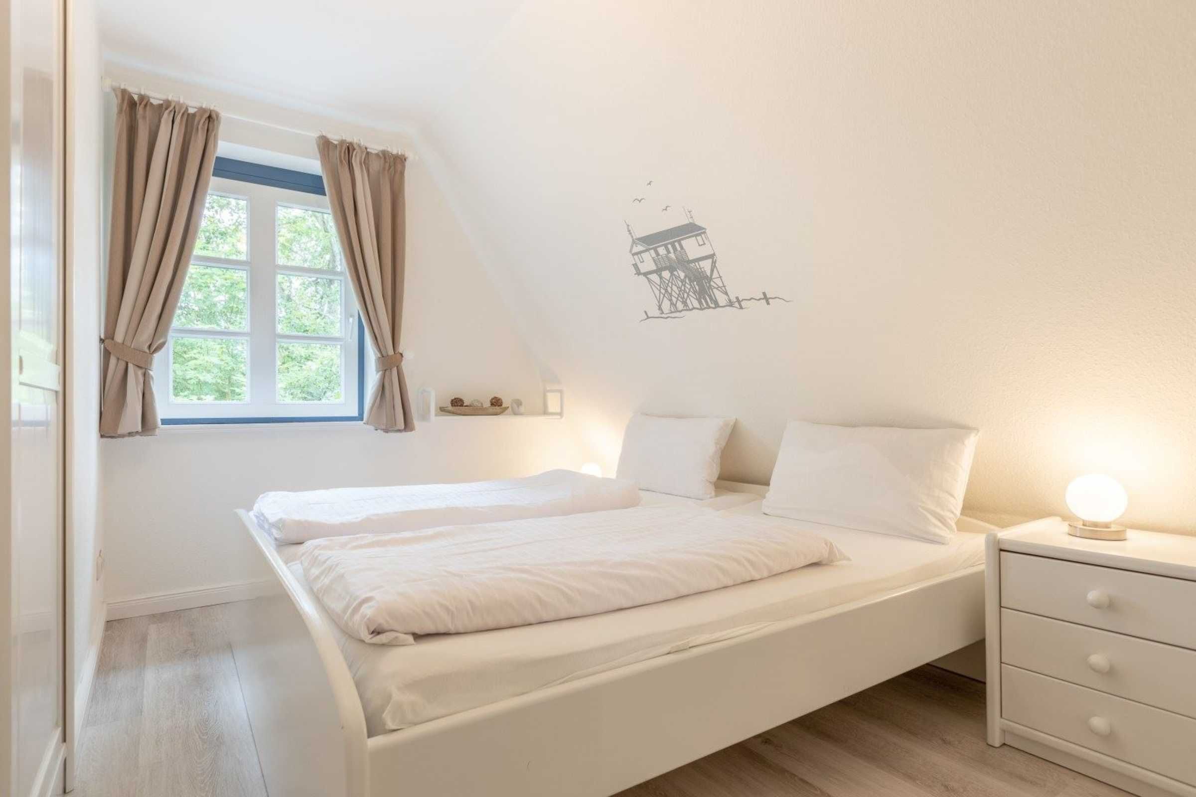 Ein Schlafzimmer mit einem Einzelbett, einem Nachttisch, einem Fenster mit Vorhängen und einer Wandsticker.