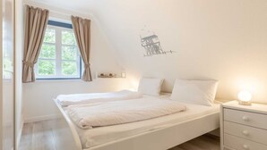 Een slaapkamer met een enkel bed, een nachtkastje, een raam met gordijnen en een muursticker.