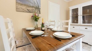 Een gedekte eettafel met borden, glazen, bestek, een champagnefles en een vaas met bloemen.