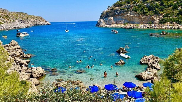 A coastal scene with clear blue waters, rocky terrain, and a few boats. - Villa Chevalier at Kiotari Beach,  south of Lindos (Dodekanissos)
