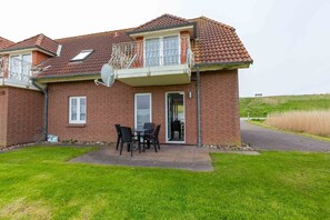 A two-story brick house with a balcony, a patio with a table and chairs, and a grassy yard.