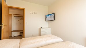 Un dormitorio con cama, armario, mesita de noche, cómoda pequeña y un cuadro enmarcado en la pared.