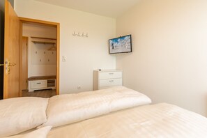 Une chambre à coucher comprenant un lit, une armoire, une table de chevet, une petite commode et un tableau encadré accroché au mur.