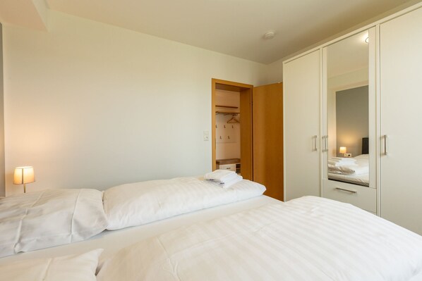A hotel room with two beds, a wardrobe, and a bedside lamp.