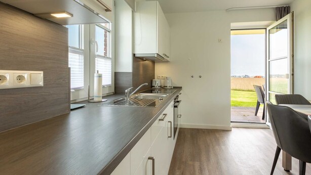 Una cocina moderna con encimera de madera oscura, armarios blancos y vistas al exterior a través de la puerta abierta.