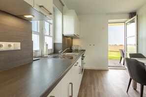 A modern kitchen with a dark wood countertop, white cabinets, and a view of the outdoors through the open door.