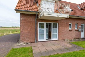 A brick building with a red-tiled roof, a balcony with white metal railings, and a sliding glass door.