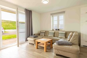 Una sala de estar moderna con un sofá color beige, una mesa de centro de madera y un puerta corrediza de vidrio que da a un balcón.