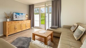 Una sala de estar moderna con un sofá, una mesa de madera, un televisor sobre un mueble de madera y un ventanal corredero que da a un balcón.
