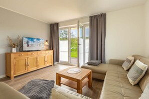 Un salon moderne avec un canapé, une table en bois, un téléviseur posé sur un meuble en bois et une porte-fenêtre coulissante donnant sur un balcon.