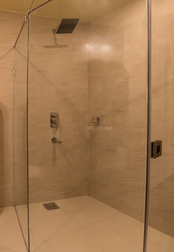 A glass-enclosed shower with a control panel, a handheld showerhead, and a floor drain.