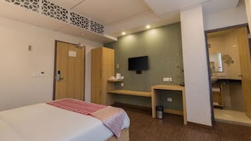 A hotel room with a bed, a desk, a TV, and a bathroom visible through an open door.