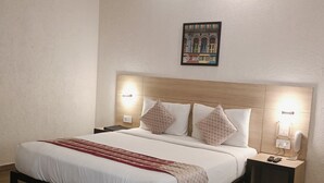 A neatly made bed with a wooden headboard, a bedside table with a lamp, and a wall-mounted picture. - The Solitaire Express (Dehradun)