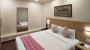 A hotel room with a large bed, a bedside table with a lamp, a wall-mounted painting, and a mirror. - The Solitaire Express (Dehradun)