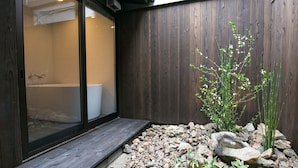 A modern bathroom with a glass shower enclosure, wooden walls, and a small rock garden with bamboo. - Nijo Yu-Rakukan (Kyoto)