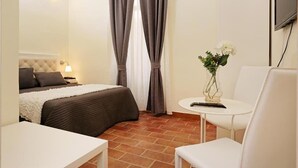 Une chambre d’hôtel avec un lit, une table de chevet avec une lampe, une petite table ronde ornée d’un vase de fleurs et une chaise.