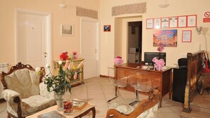 Un hall d’hôtel avec un comptoir d’accueil, un canapé, un fauteuil et une table ornée d’un vase de fleurs.