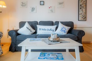 A living room with a grey sofa, three cushions with text, a white coffee table with a tray, and wall art.