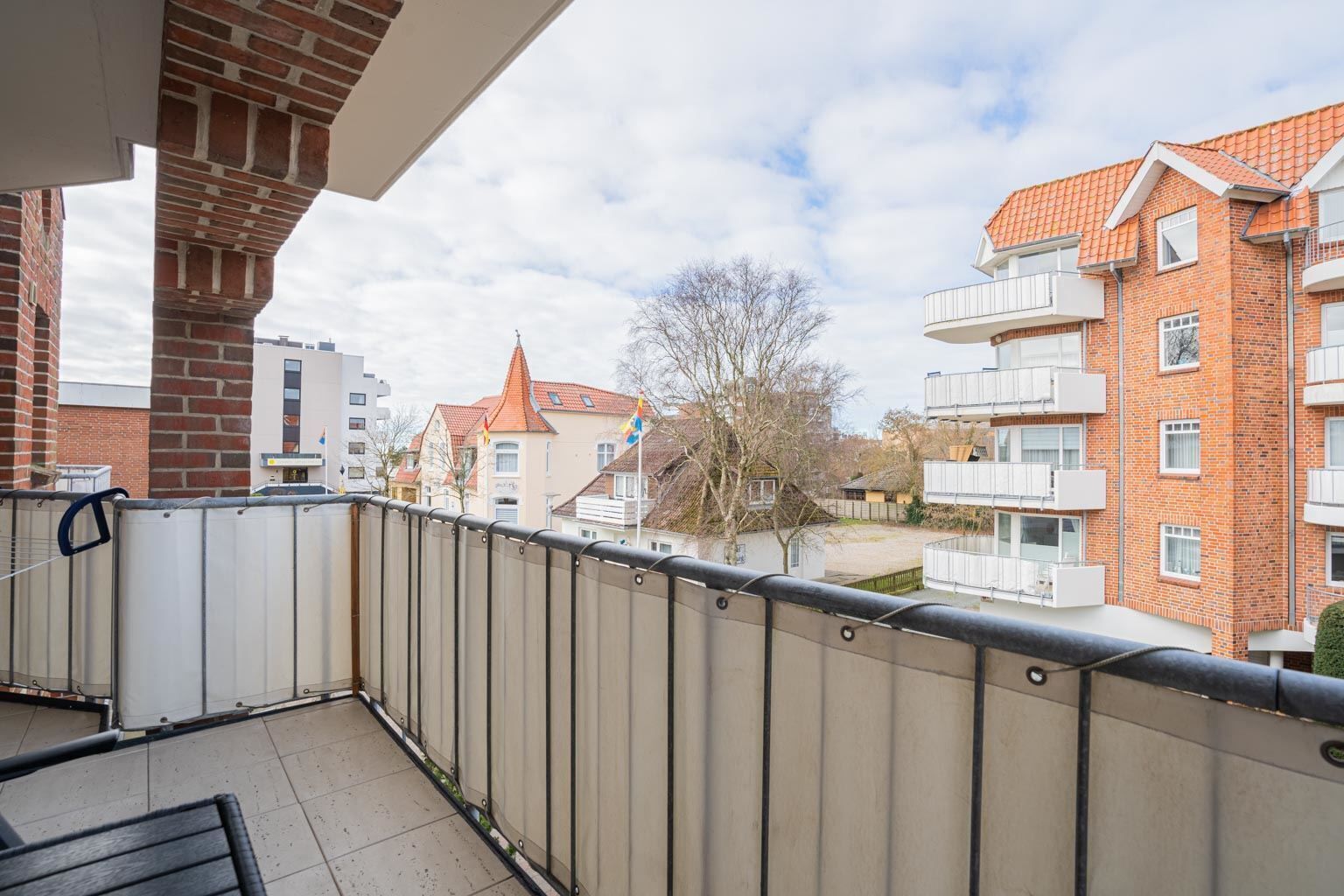 En balkon med udsigt til en murstensbygning og et træ.