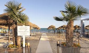 A beach pathway leading to a private beach area with thatched umbrellas and sun loungers. - Hotel Elite (Jesolo)