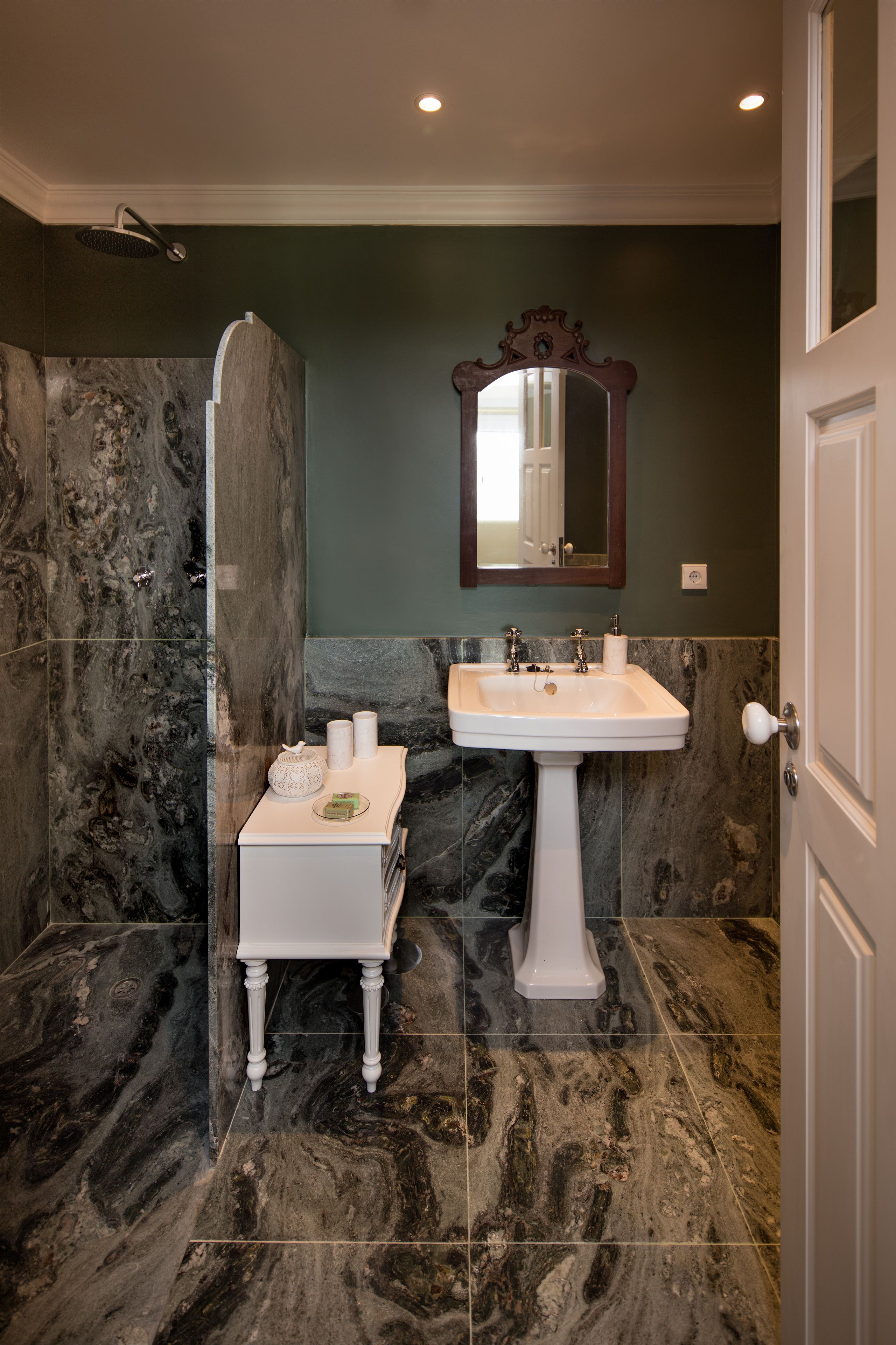 Un baño con ducha de mármol, lavabo pedestal y tocador con artículos de aseo.