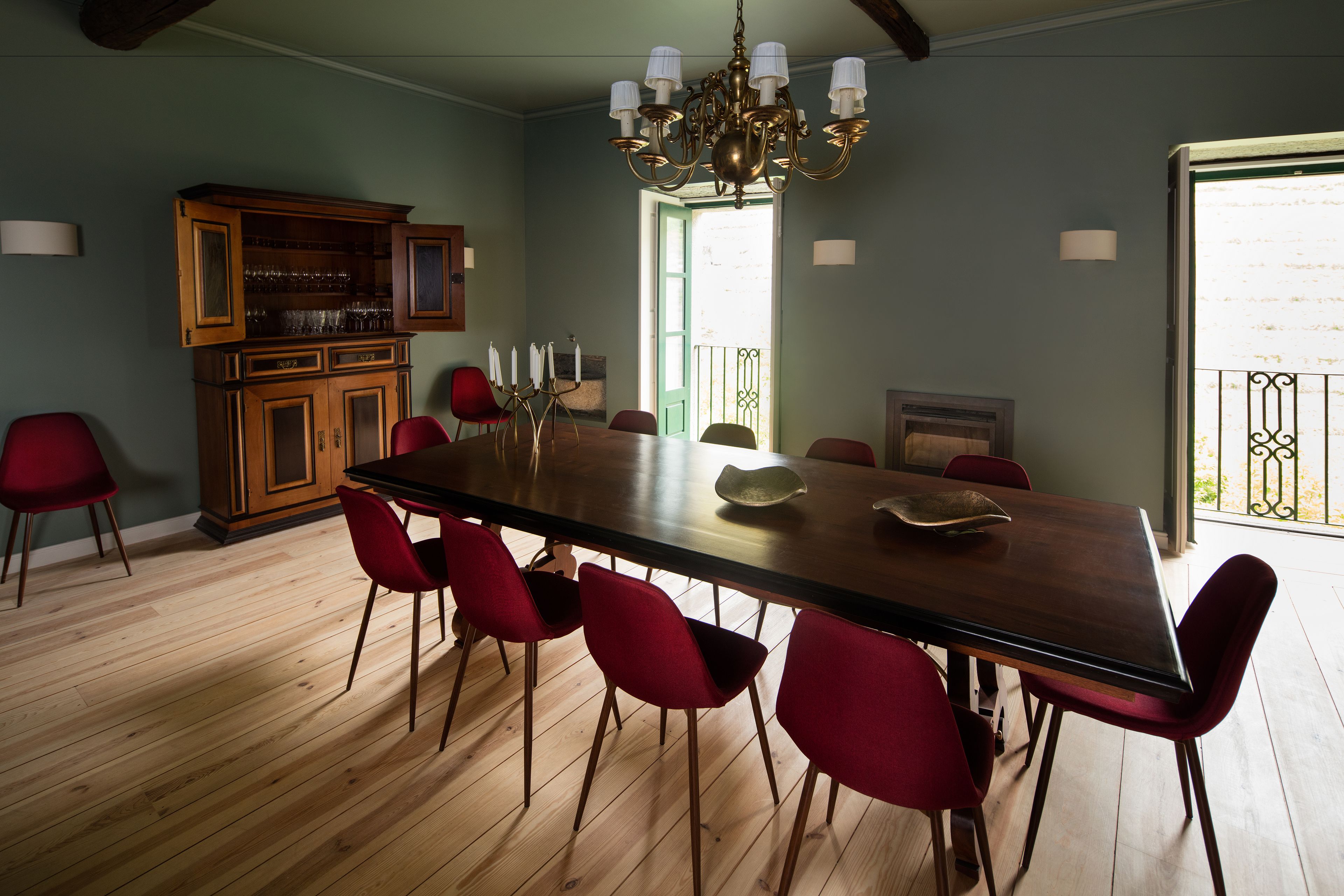 A dining area with a wooden table, red chairs, a chandelier, and a wooden cabinet with glass doors.