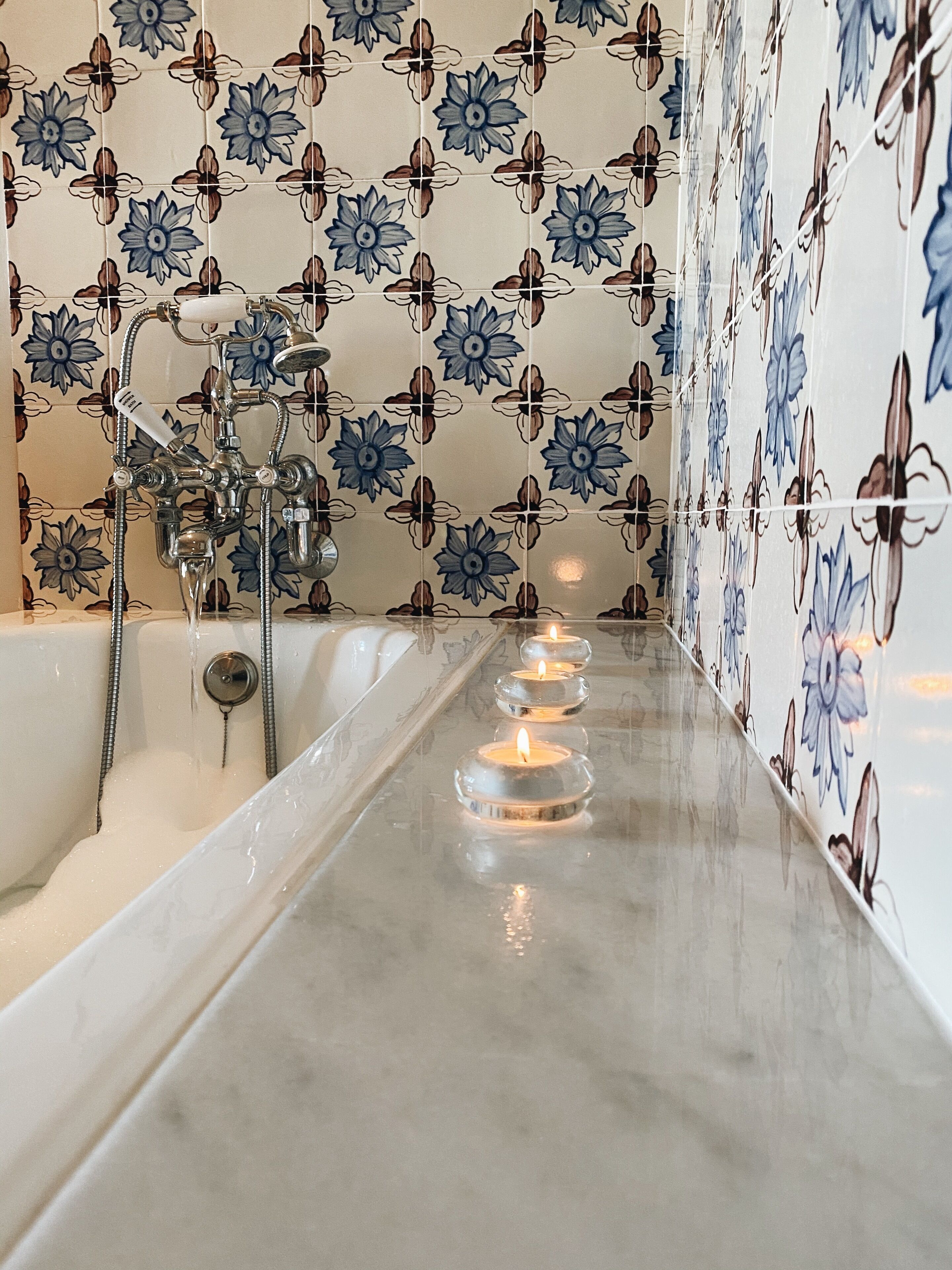 Une salle de bain avec une baignoire, une douche et trois bougies allumées posées sur le sol.