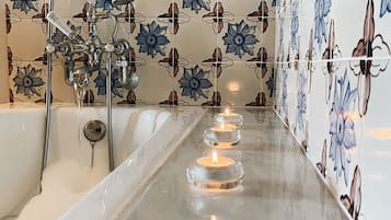Une salle de bain avec une baignoire, une douche et trois bougies allumées posées sur le sol.