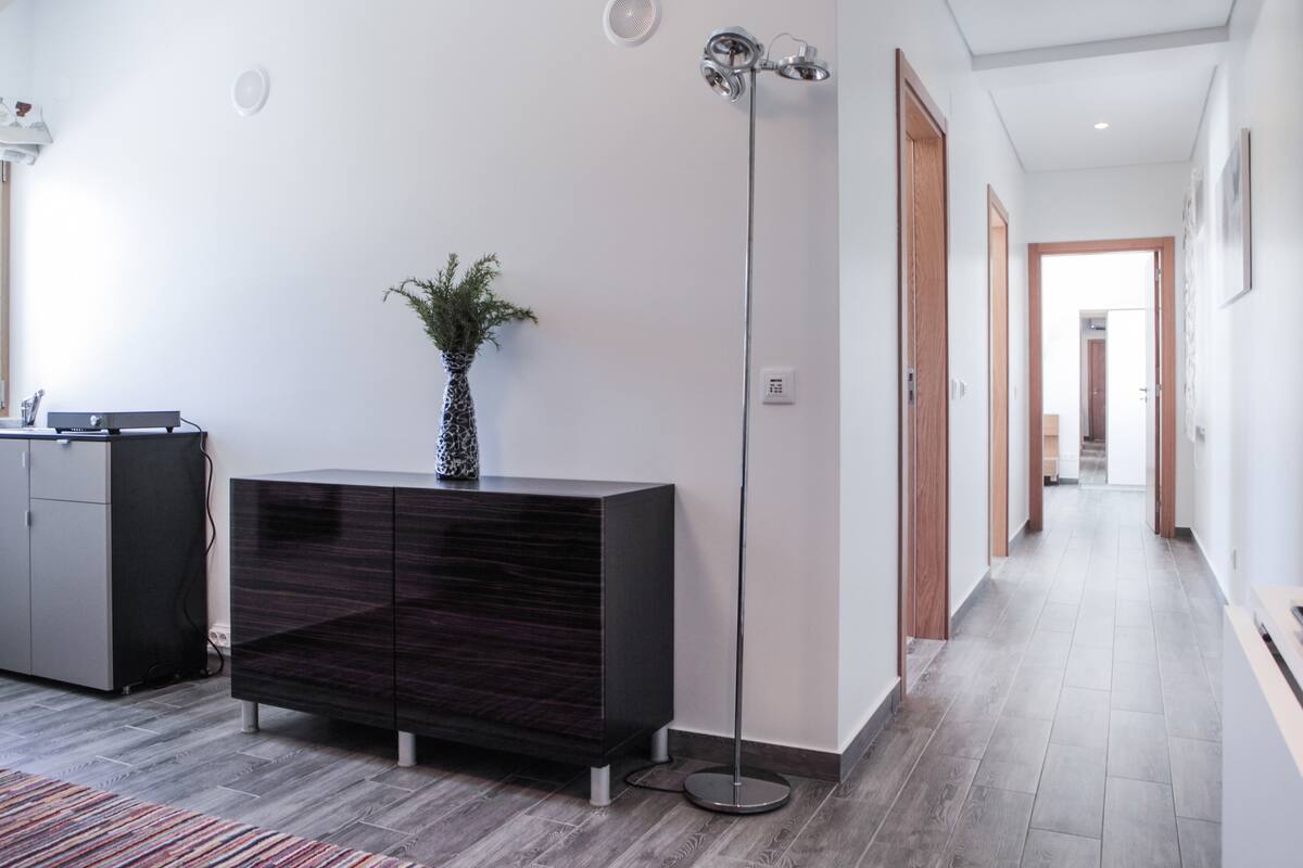 Una sala de estar moderna con un mueble de madera oscura, una lámpara de pie alta y una planta en maceta.