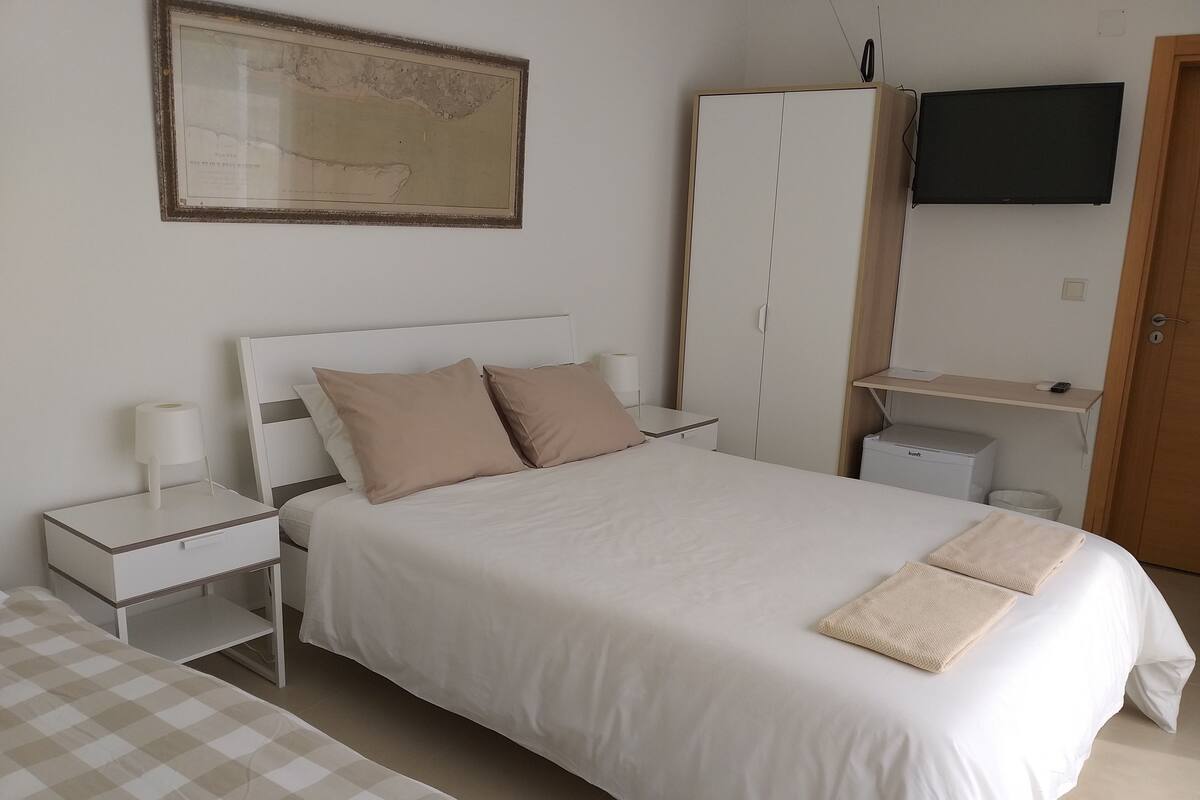 Un dormitorio ordenado con cama, mesitas de noche, televisor y armario.
