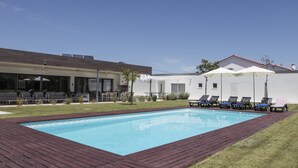 Une piscine avec une terrasse en bois, des chaises longues et un bâtiment doté d’un espace extérieur aménagé pour s’asseoir.