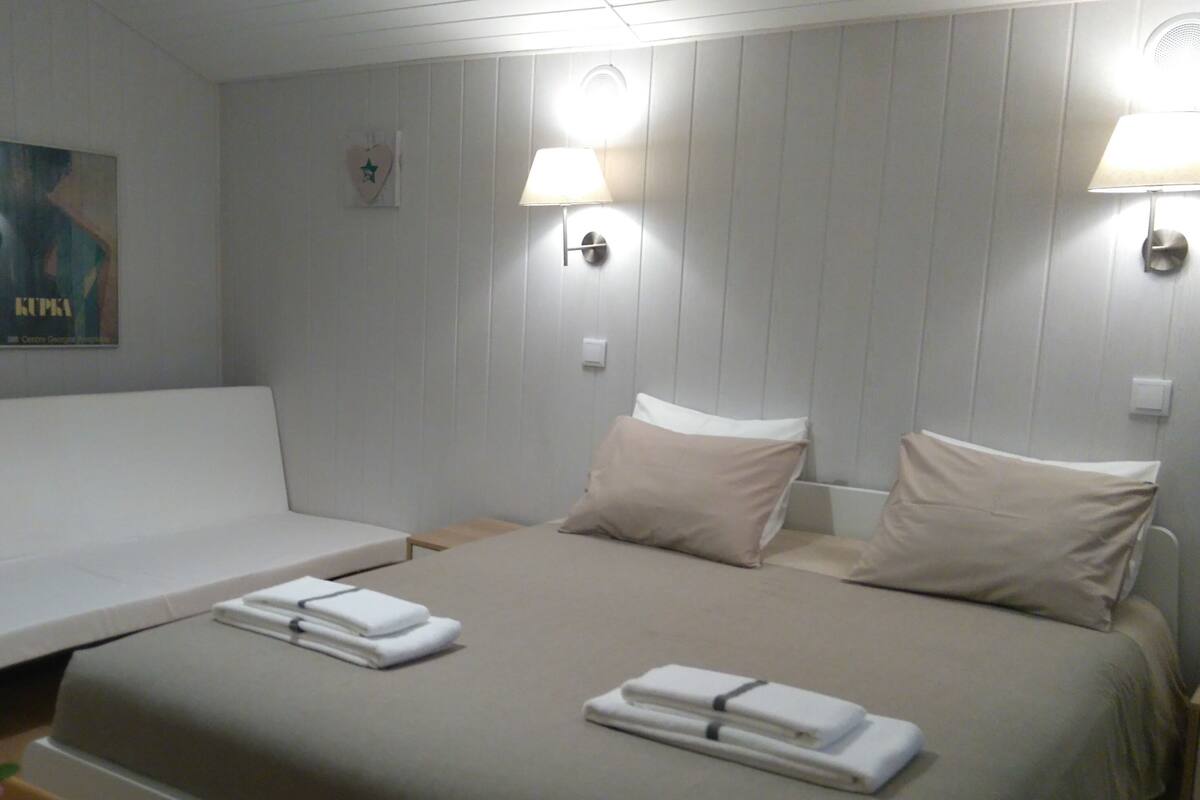 Habitación de hotel con cama, dos mesitas de noche, una silla y una lámpara de pared.