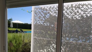 Une vue à travers une fenêtre ornée d’un paravent décoratif, avec une piscine et des chaises longues.