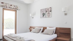 Une chambre moderne avec un lit en bois, du linge de lit blanc et une vue sur un arbre à l’extérieur.