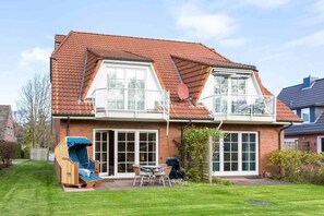 A two-story house with a red-tiled roof, large windows, and a patio area with outdoor furniture.