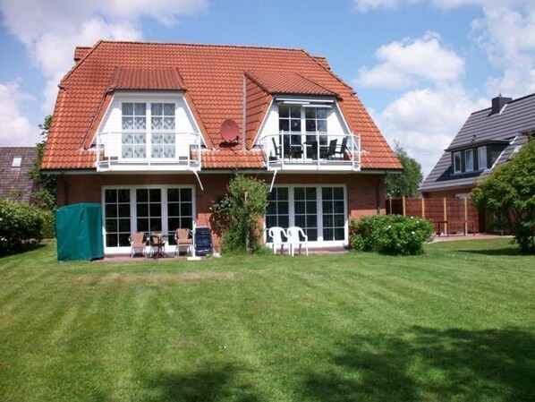 A two-story house with a red-tiled roof, a balcony with outdoor seating, and a well-maintained lawn.