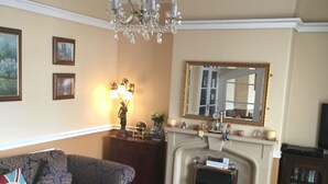 A living room with patterned sofas, a chandelier, a fireplace, and a mirror on the wall. - White Lodge Guest House (Skegness)
