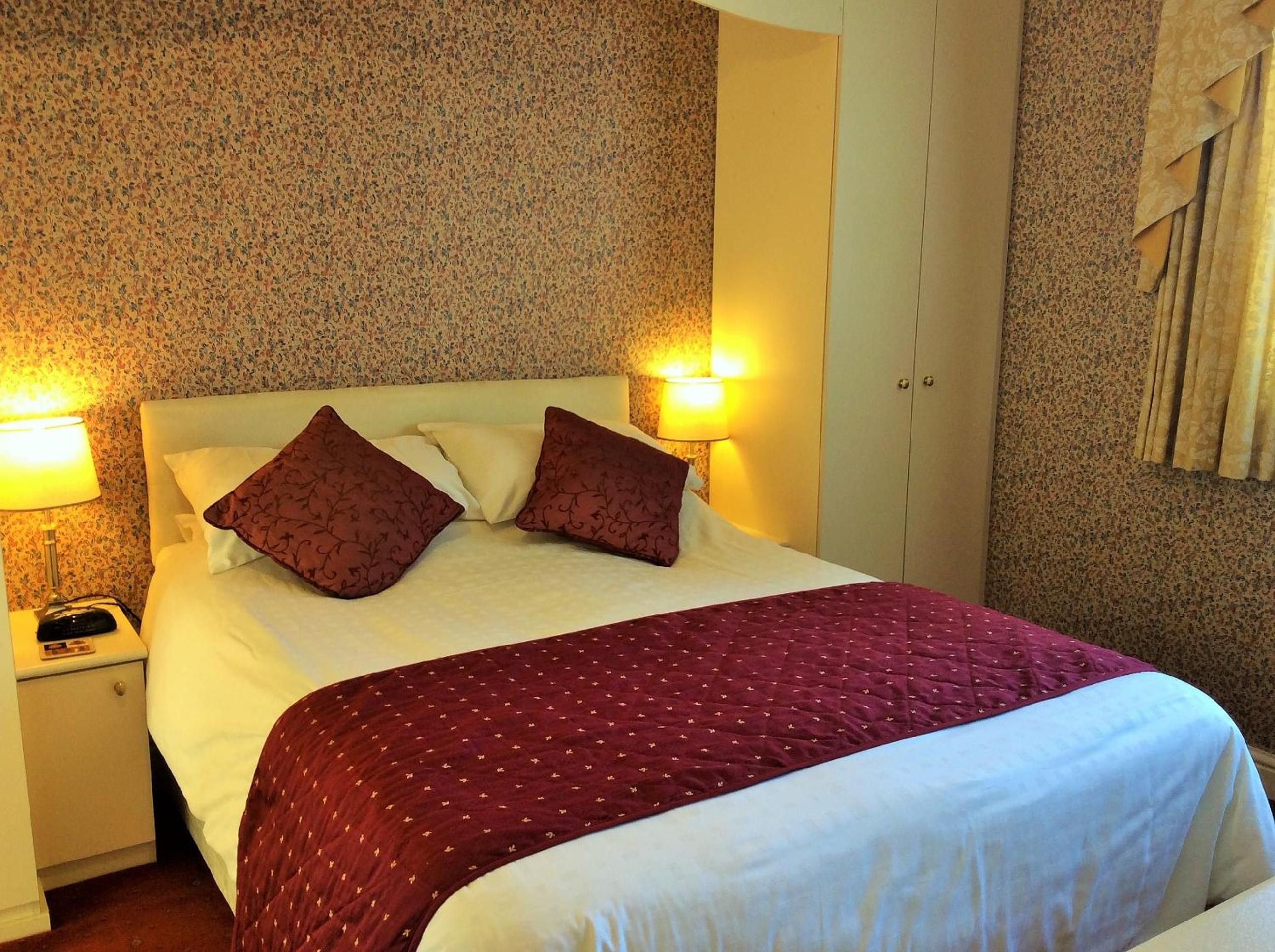 A hotel room with a bed, two bedside lamps, a nightstand, and a patterned wall.