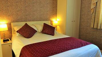 A hotel room with a bed, two bedside lamps, a nightstand, and a patterned wall.