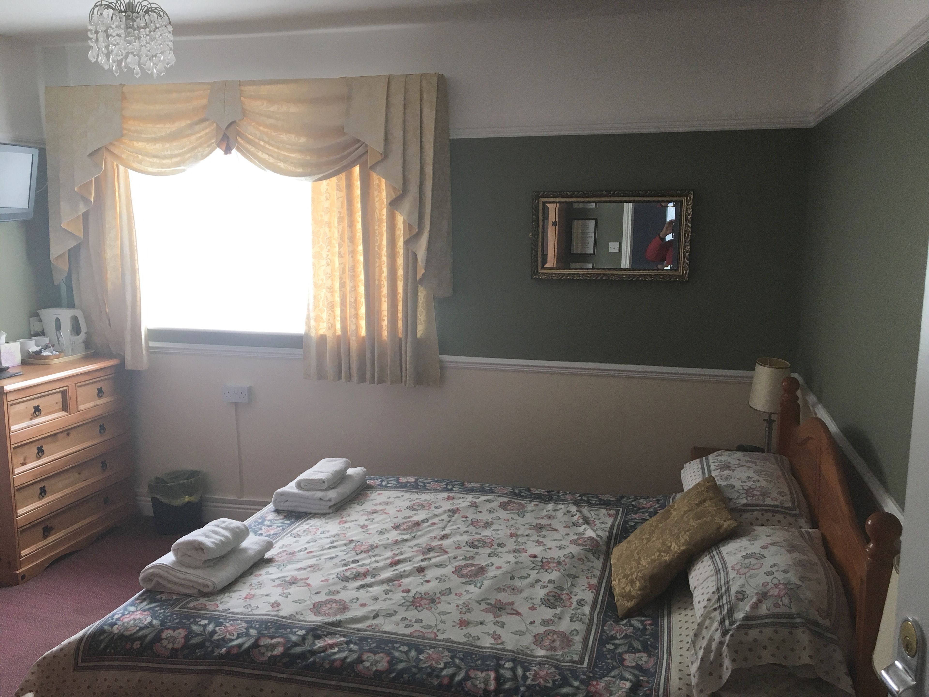 Une chambre à coucher avec un lit, une commode, un miroir et une fenêtre avec des rideaux.