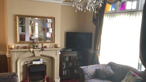 A living room with a fireplace, a television, and two patterned sofas. - White Lodge Guest House (Skegness)