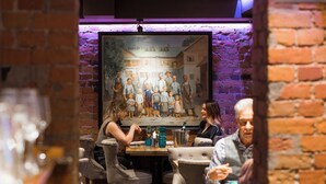 A restaurant with brick walls and a large painting of a family. There are tables and chairs for dining. - Harmooni Suites (Jyväskylä)