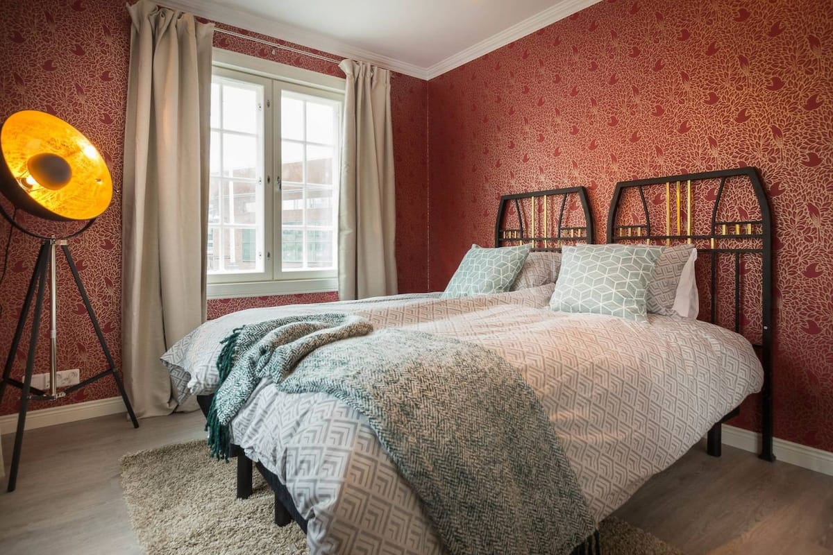 A bedroom with a bed, a floor lamp, and a window with curtains.