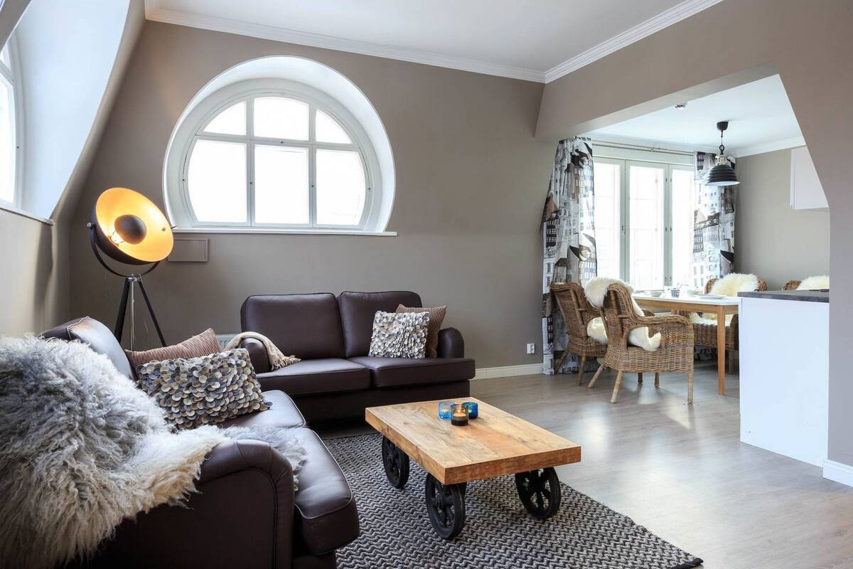 A modern living room with a brown leather sofa, a wooden coffee table, and a large window.